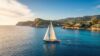 A classic sailing yacht anchored in a deep turquoise cove flanked by sheer white limestone cliffs in the Mediterranean