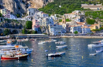 Cliffside pastel buildings overlooking the Positano harbor on the Amalfi Coast with yachts anchored in calm blue water.