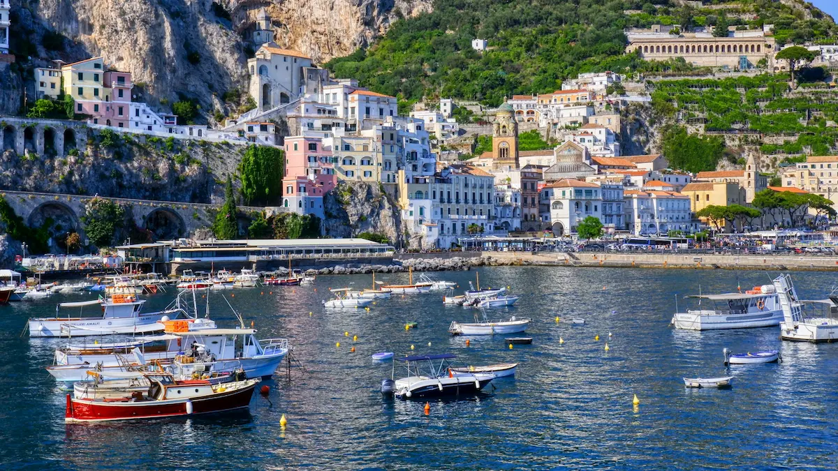 Cliffside pastel buildings overlooking the Positano harbor on the Amalfi Coast with yachts anchored in calm blue water.