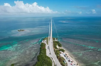 Aerial view of the Overseas Highway bridge over turquoise water in the Florida Keys, showing shallow reefs and small islands.