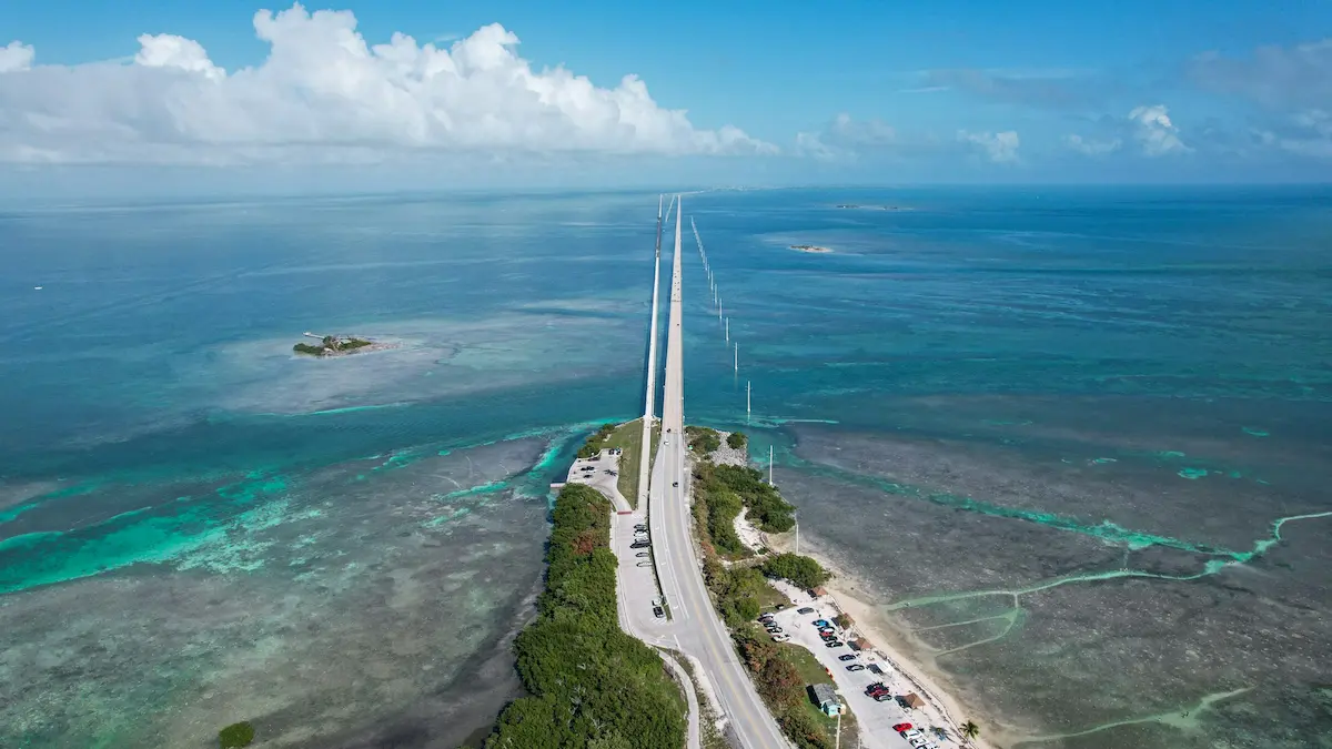 Aerial view of the Overseas Highway bridge over turquoise water in the Florida Keys, showing shallow reefs and small islands.