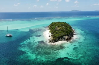 Small tropical island in the Tobago Cays surrounded by turquoise water with a catamaran anchored nearby under clear Caribbean skies.