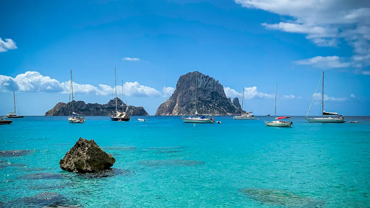 Turquoise bay with moored sailboats and Es Vedrà rock off Ibiza, Balearic Islands