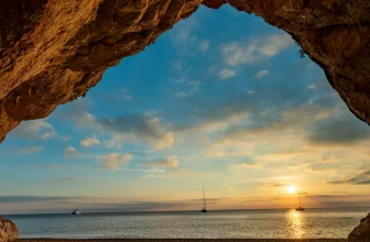 View through a sea cave to sailboats at sunset off Cala Luna, Sardinia