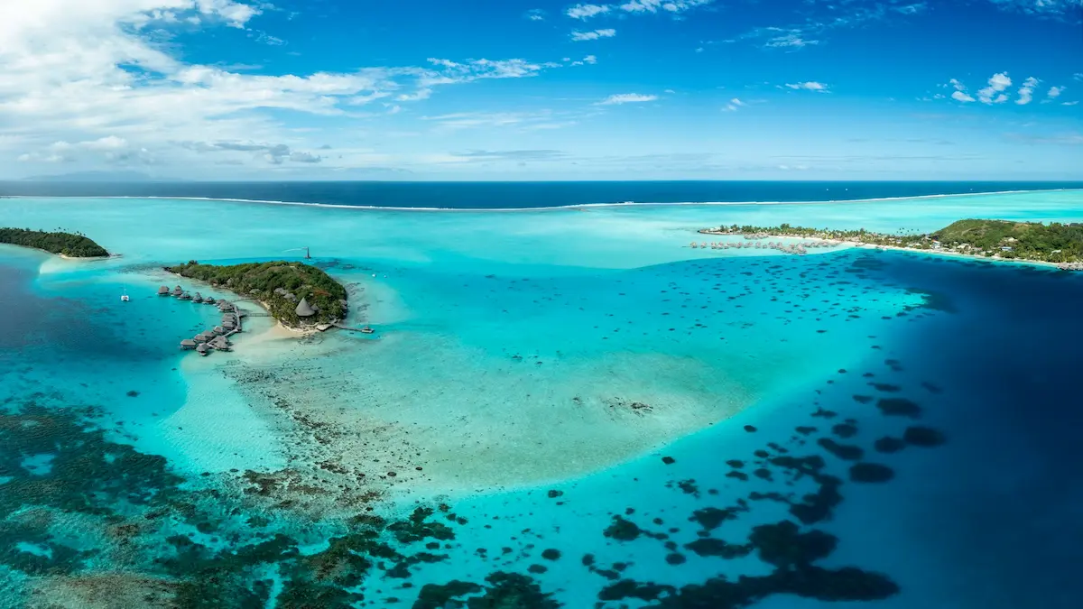 Aerial view of turquoise lagoon, motus and anchored boats at Bora‑Bora, French Polynesia
