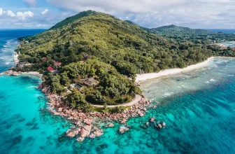 Aerial view of La Digue, Seychelles with granite rocks, white-sand beaches, turquoise water, lush vegetation, and coastal buildings near the shoreline.