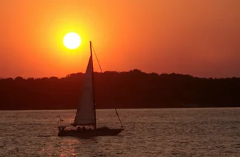 A luxury sailing yacht cruising past the historic Castle Hill Lighthouse in Newport, Rhode Island during a summer yacht charter.